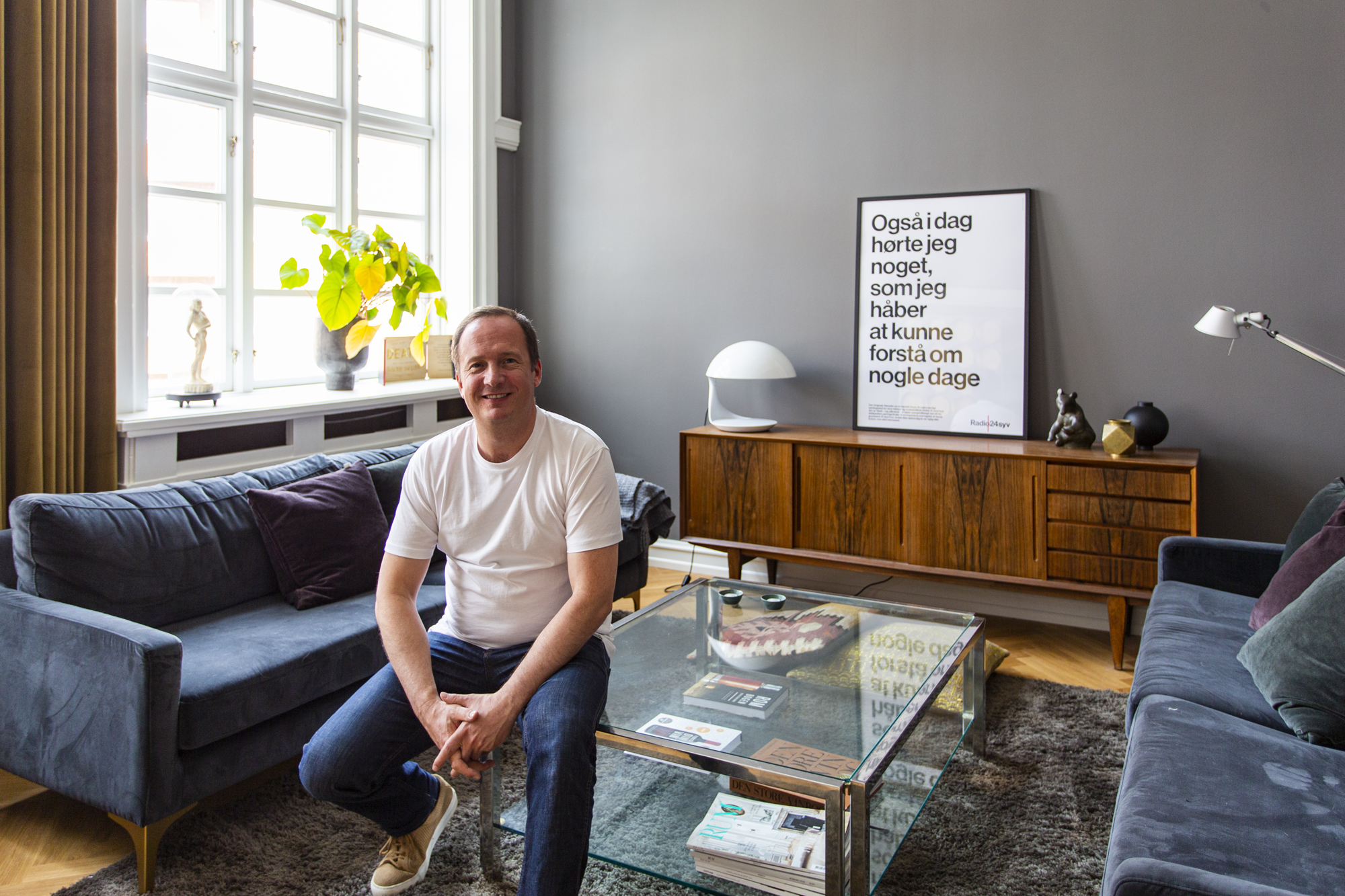 To blå sofaer og mand sidder på glasbord
